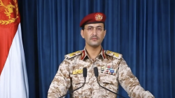 Houthi military spokesman Yahya Saree delivering a televised statement beside the Yemeni flag