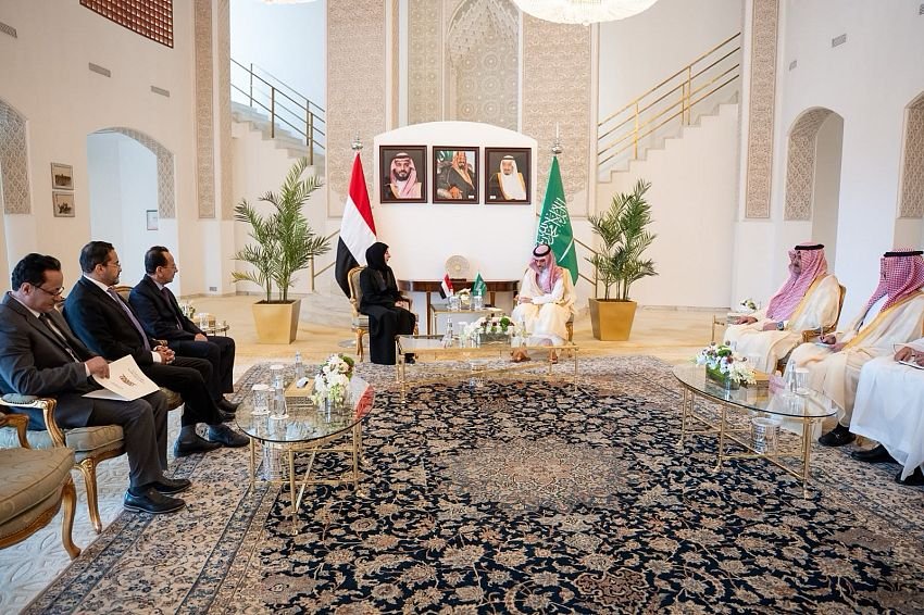 Yemeni Foreign Minister Afrah al-Zouba seated with Saudi Foreign Minister Prince Faisal bin Farhan and delegations beneath Yemeni and Saudi flags during talks in Riyadh