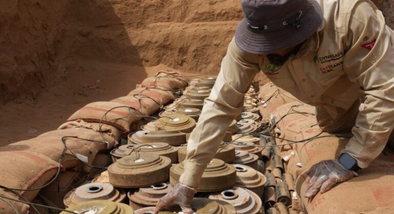A MASAM demining technician kneels beside rows of recovered landmines and unexploded ordnance laid out on the ground in Yemen