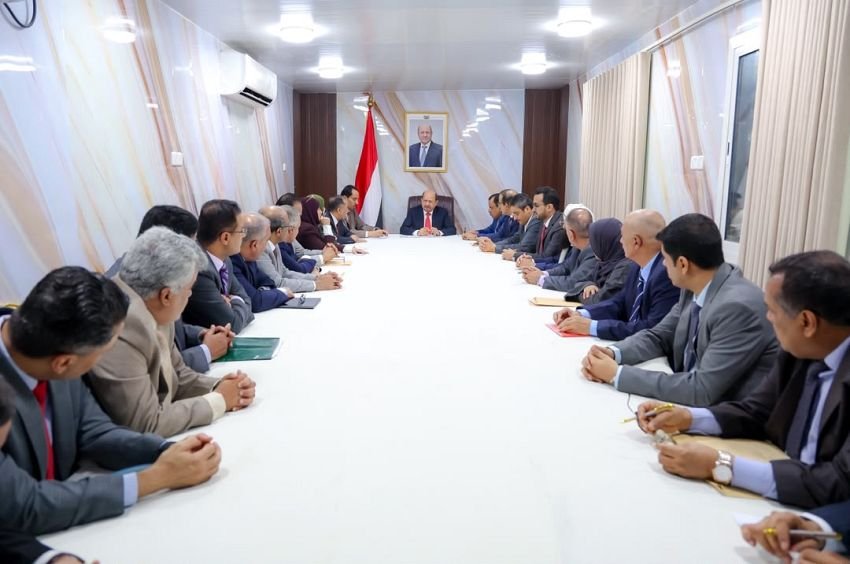 Yemeni ministers seated around a long table during a Council of Ministers meeting in Aden, with the Yemeni flag and a portrait of the president behind the chair