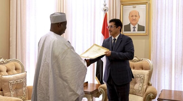Nigeria's non-resident ambassador Dr. Yakoub An Gambo hands a folder containing a copy of his credentials to a Yemeni foreign ministry official, beside a Yemeni flag and a portrait of the president