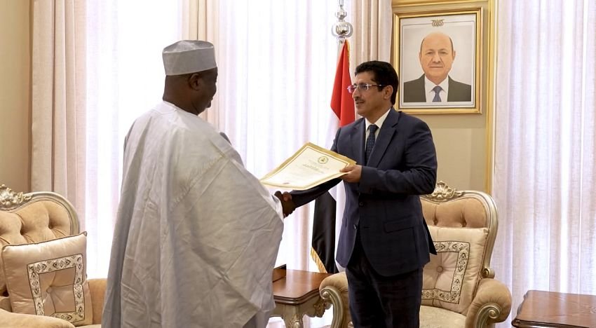 Nigeria's non-resident ambassador Dr. Yakoub An Gambo hands a folder containing a copy of his credentials to a Yemeni foreign ministry official, beside a Yemeni flag and a portrait of the president