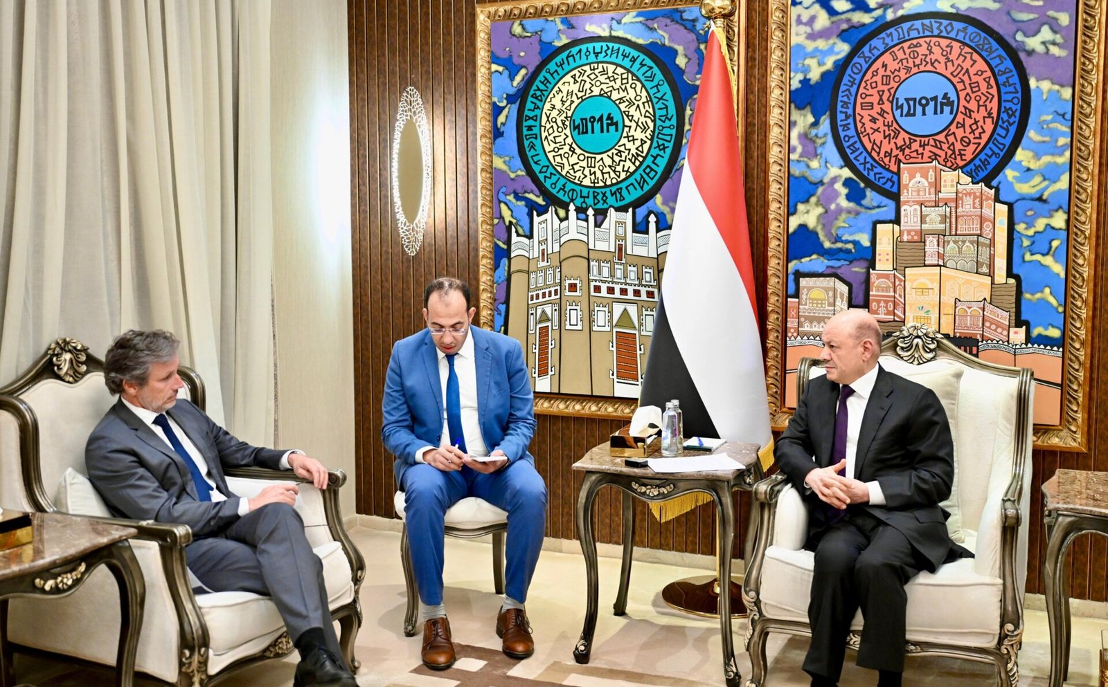 President Rashad al-Alimi seated with a German defence delegation in a Yemeni reception room with the national flag behind him