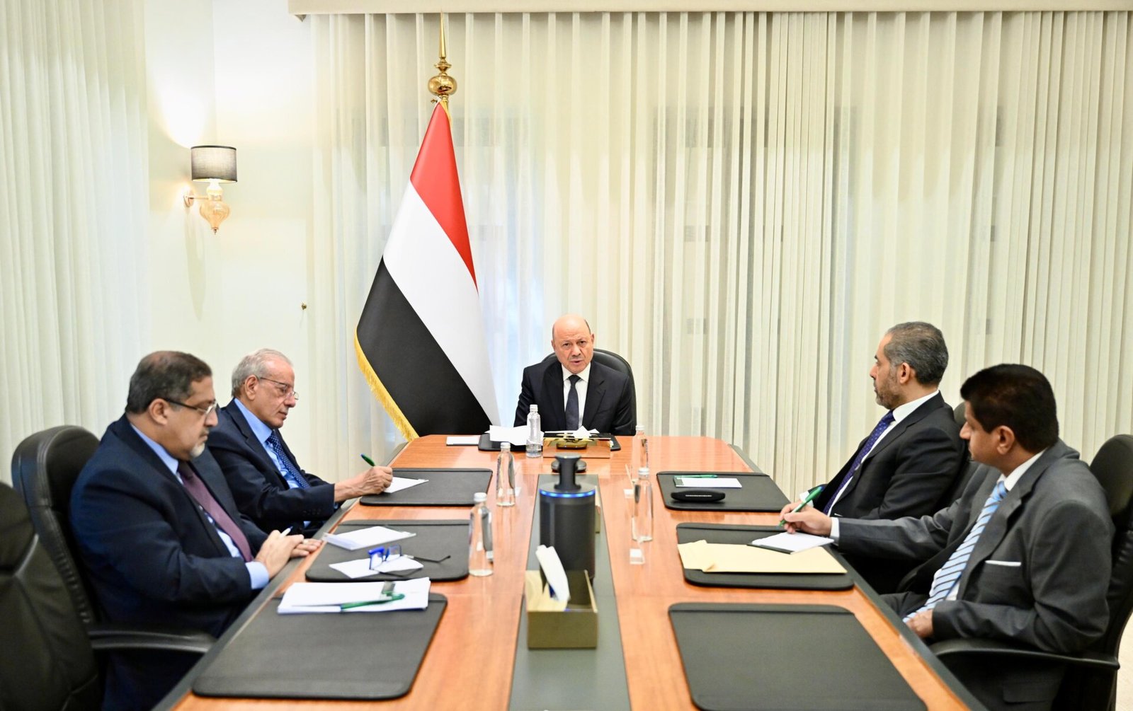 President Rashad al-Alimi chairs a meeting of Yemen's Supreme Committee for Combating Smuggling, seated before the Yemeni flag.