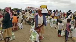 Yemeni civilians carrying sacks of food aid at a distribution point