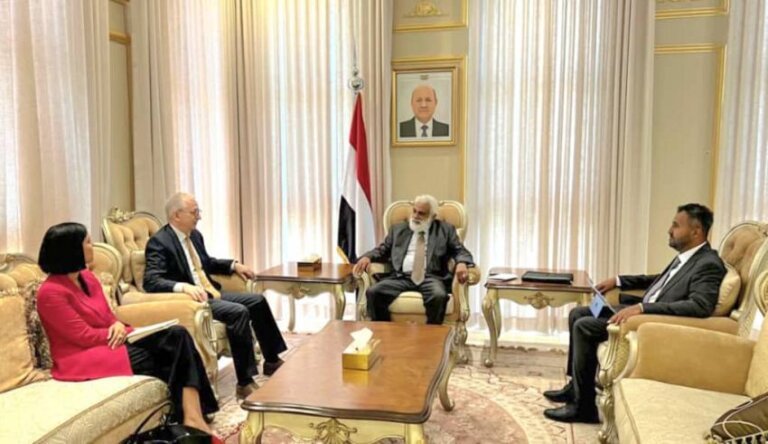 Yemeni planning minister seated at a meeting table beside the Yemeni flag