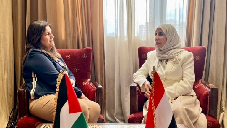 Yemen's foreign minister meets her Palestinian counterpart in Cairo, seated beside the Palestinian and Yemeni flags