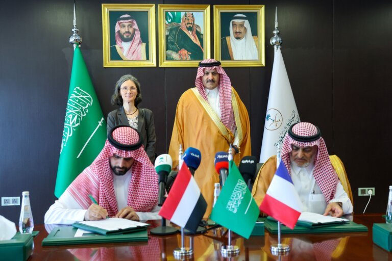 Officials sign a water project agreement at a table bearing Saudi, Yemeni and French flags