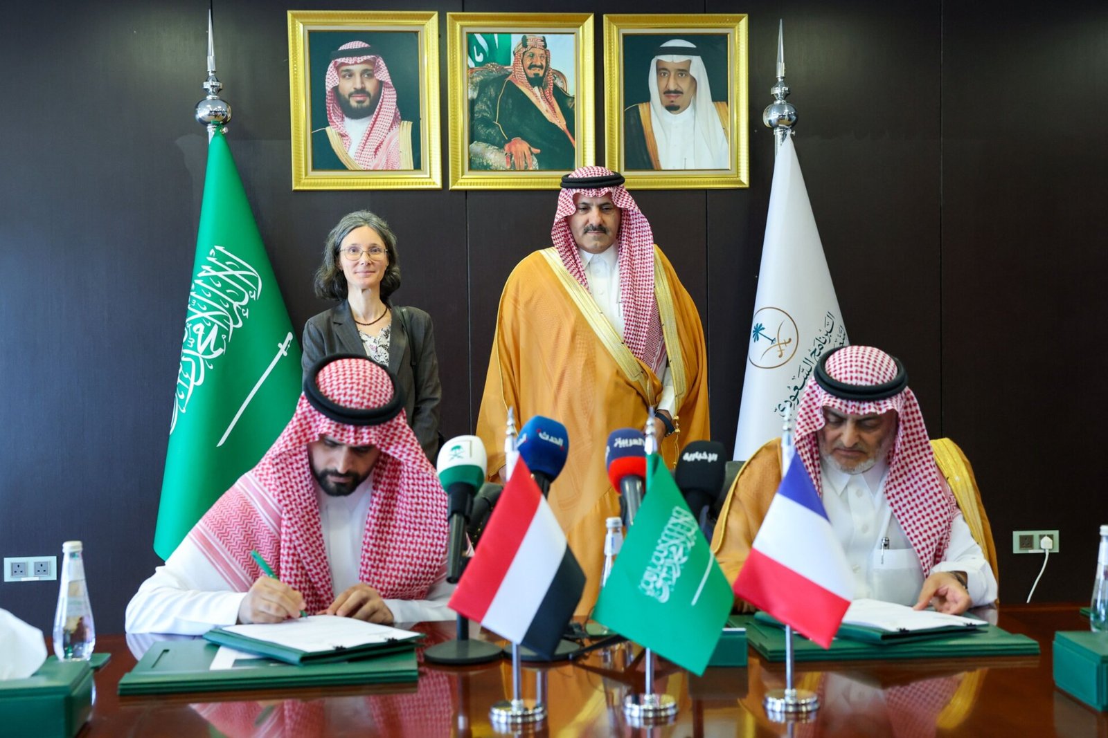 Officials sign a water project agreement at a table bearing Saudi, Yemeni and French flags