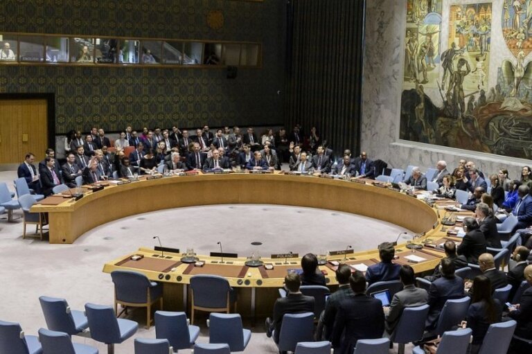 Delegates seated around the horseshoe table in the United Nations Security Council chamber during a session