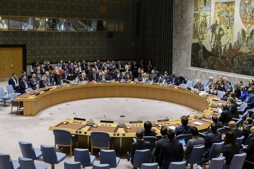Delegates seated around the horseshoe table in the United Nations Security Council chamber during a session