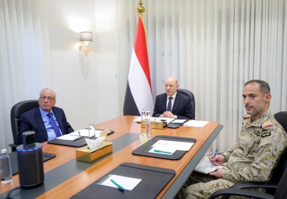 President Rashad al-Alimi chairs a meeting with Yemeni officials and a military commander beside the national flag