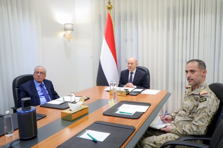 President Rashad al-Alimi chairs a meeting with Yemeni officials and a military commander beside the national flag