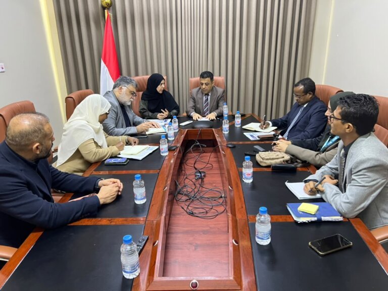 Yemeni officials and WHO representatives seated around a meeting table in Aden beneath Yemeni flags