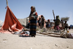 A woman and children stand beside a makeshift tent pitched on open ground at a displacement site in Yemen.