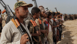 Yemeni fighters stand in a line holding rifles on open ground during operations on the western Taiz front