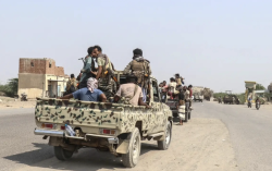 Fighters in pickup trucks move along a road on the front line in southwest Yemen