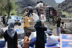Displaced Yemeni families unload relief supplies from a truck in a mountainous area