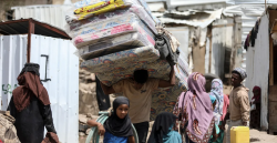 A displaced Yemeni family carries mattresses and belongings past makeshift shelters