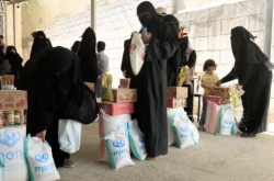 Women and children collect sacks and boxes of food aid at a humanitarian distribution point in Yemen