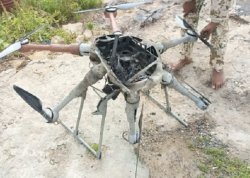 Wreckage of a downed multirotor drone on the ground with soldiers standing beside it