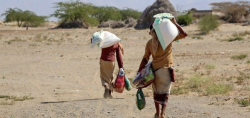 Two displaced people carry sacks of aid across open ground in Yemen