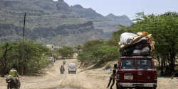 A loaded pickup truck and people on foot moving along a mountain road in Yemen as families flee fighting