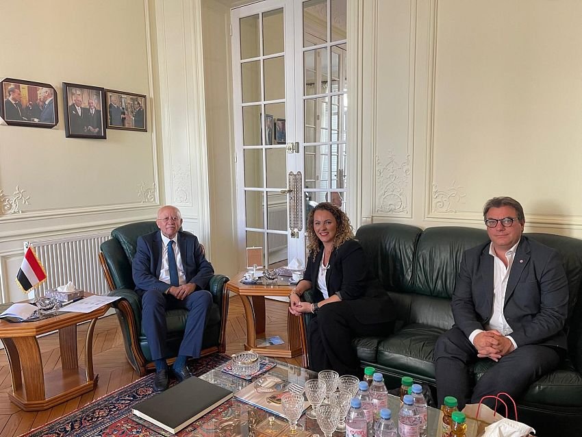 Yemen’s ambassador to France seated with two French National Assembly deputies at the embassy in Paris, a Yemeni flag on the table