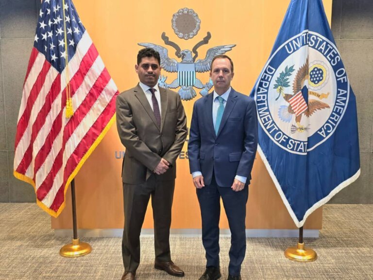 Yemen's human rights minister Mashdal Omar stands with a U.S. official in front of American and Yemeni flags in Geneva.