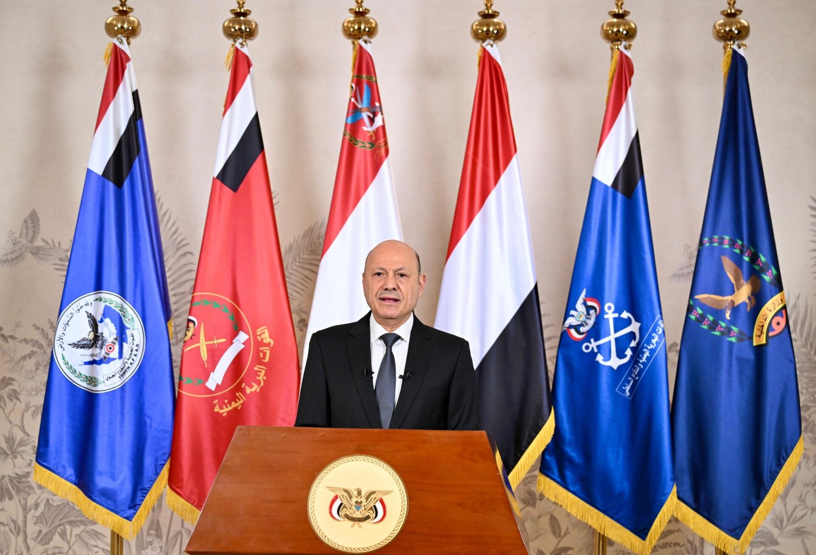 Rashad al-Alimi, chairman of Yemen's Presidential Leadership Council, delivers a televised address at a podium bearing the Yemeni state emblem, flanked by national and armed forces flags.