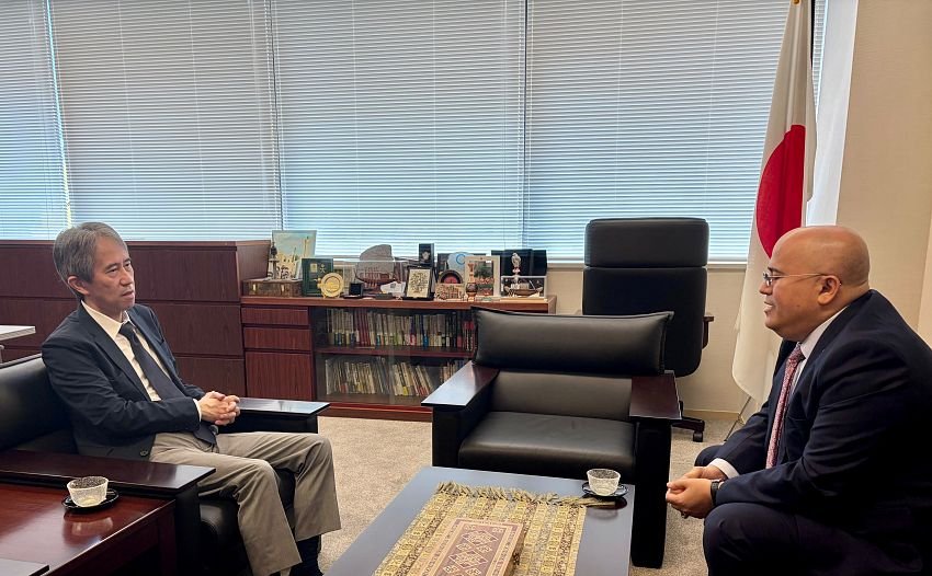 Two diplomats seated facing each other in a Tokyo office with a Japanese flag behind them