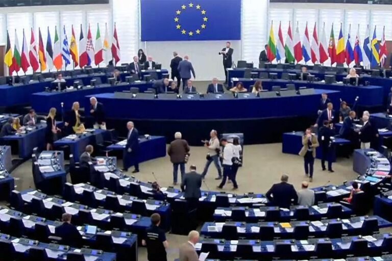 Members of the European Parliament seated in the plenary chamber in Strasbourg beneath rows of European Union and member state flags