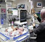 A nurse in a headscarf tends to a newborn lying in an incubator in a hospital neonatal unit.