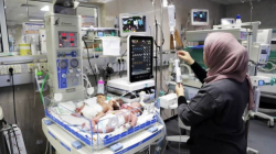 A nurse in a headscarf tends to a newborn lying in an incubator in a hospital neonatal unit.