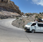 A minibus loaded with luggage rounds a switchback on a mountain road cut into rock in southern Yemen.