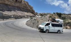 A minibus loaded with luggage rounds a switchback on a mountain road cut into rock in southern Yemen.