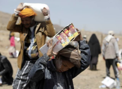 People carry sacks and boxes of food aid on their heads at a distribution site in Yemen